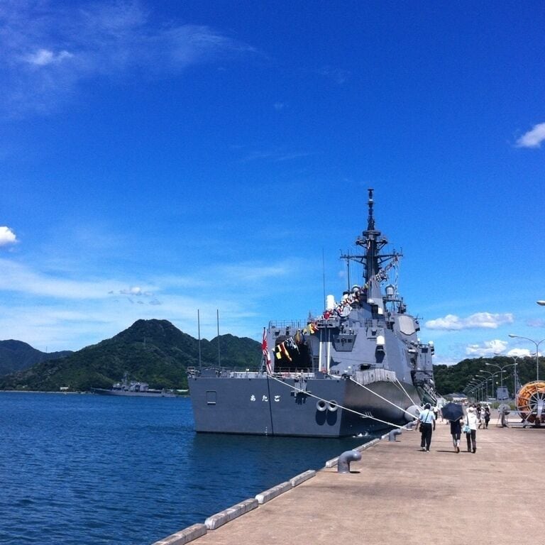 A naval ship docked at a pier with mountains in the background.