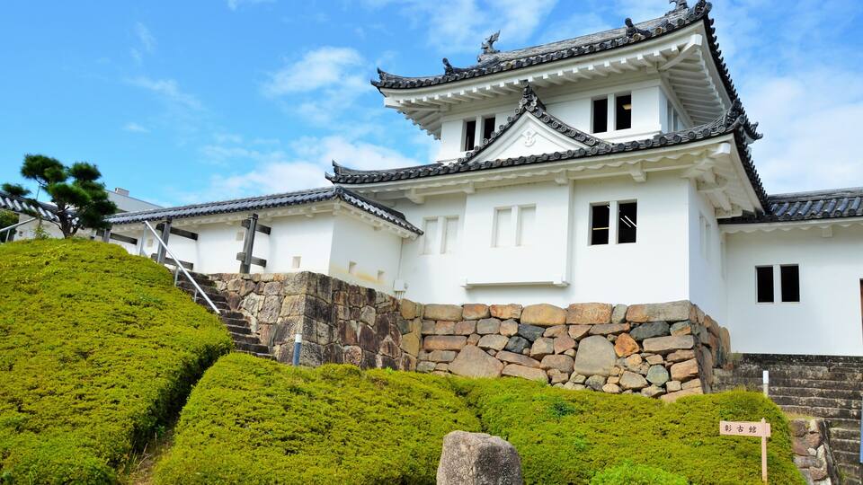 A traditional Japanese castle with white walls, black tiled roofs, and stone walls.