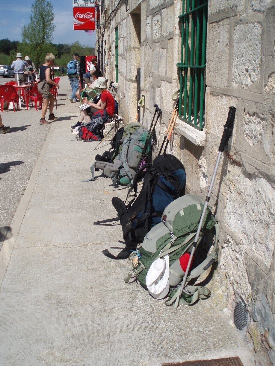 A row of backpacks and hiking poles leaning against a stone building with a Coca-Cola sign.