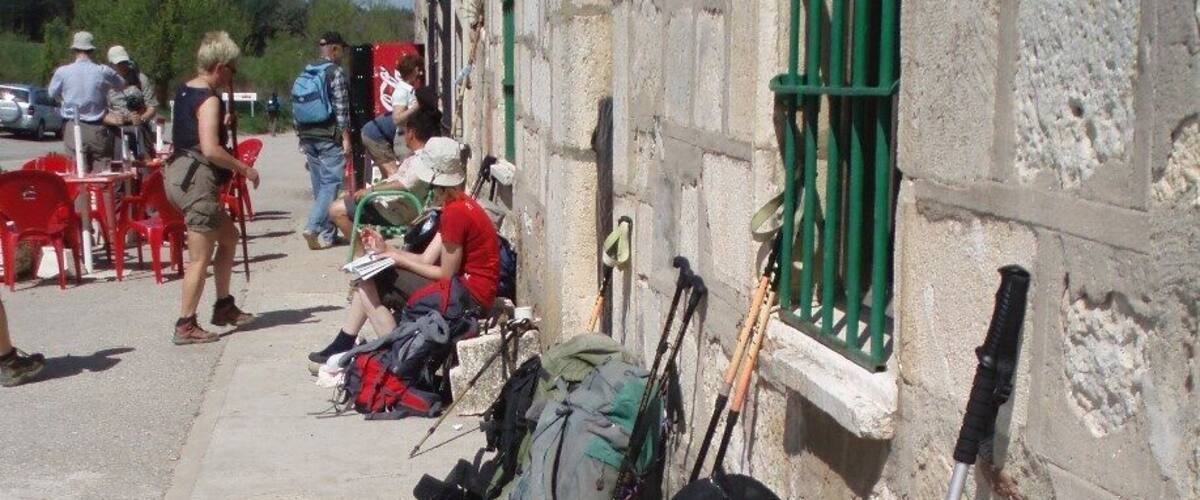 A row of backpacks and hiking poles leaning against a stone building with a Coca-Cola sign.
