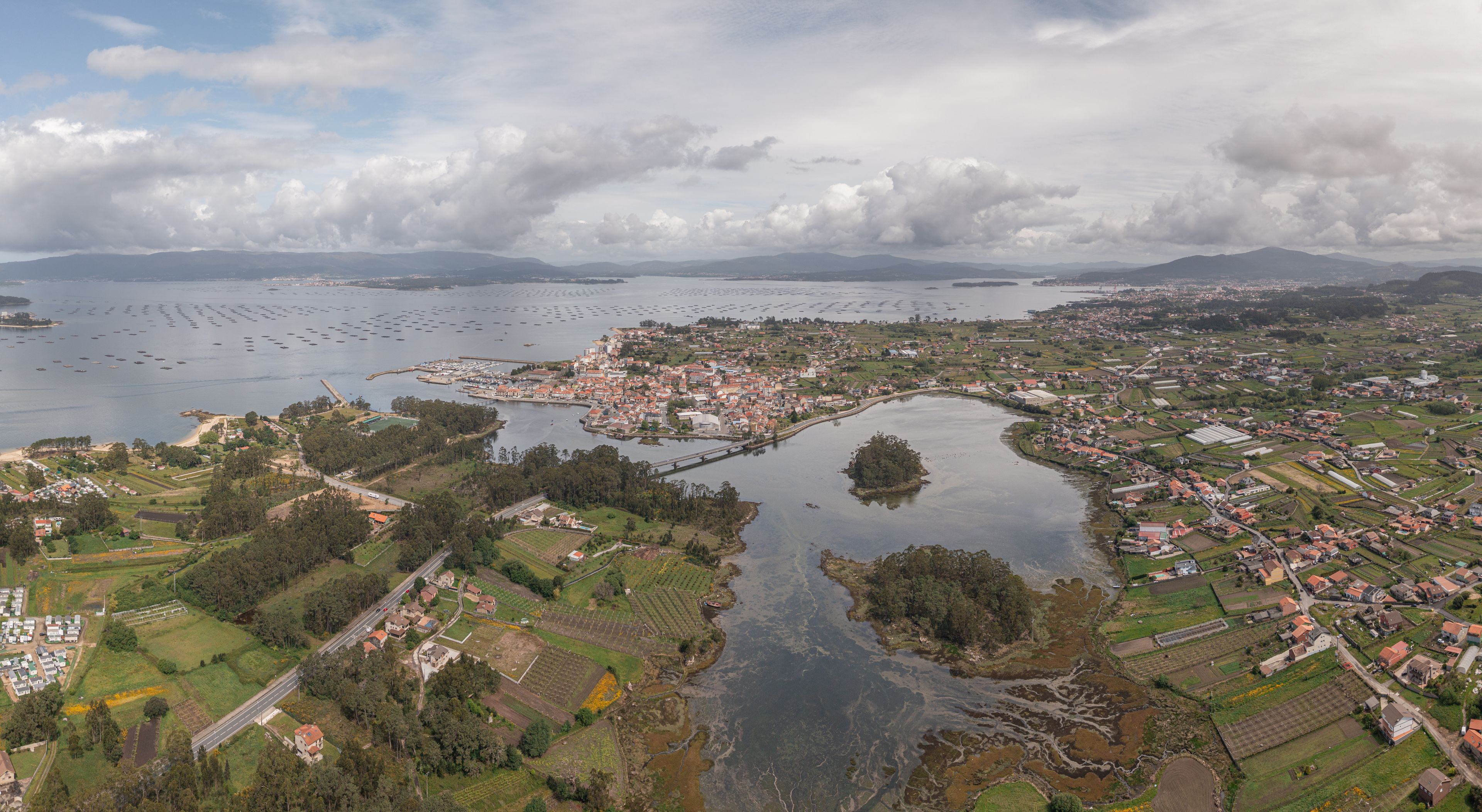 Aerial view of Vilanova de Arousa featuring the coastal town, the bay with mussel rafts, lush fields, and a bridge crossing the estuary in Vilanova de Arousa, Pontevedra, Spain.