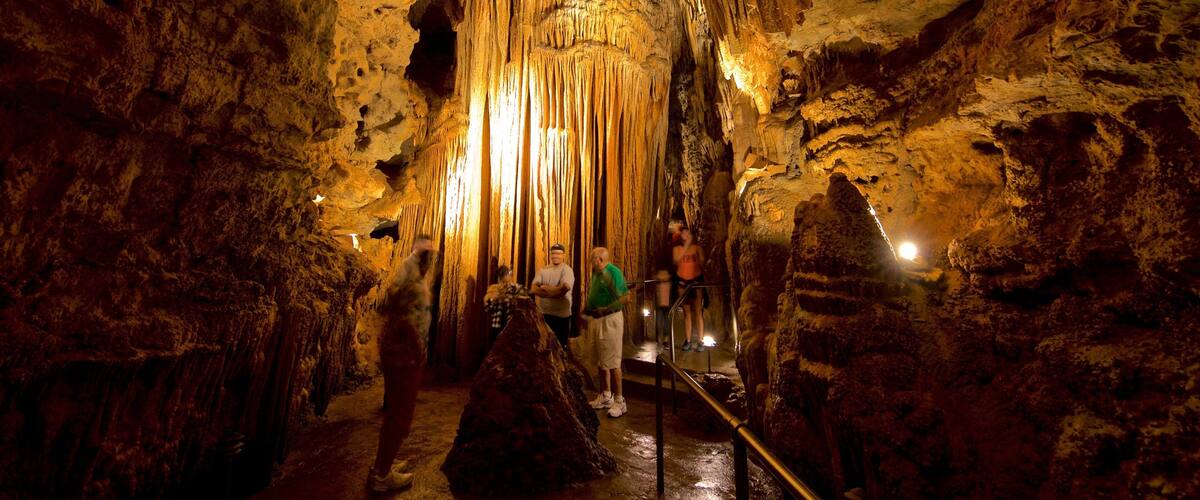 Una cueva con estalactitas y estalagmitas, iluminada por luces artificiales.
