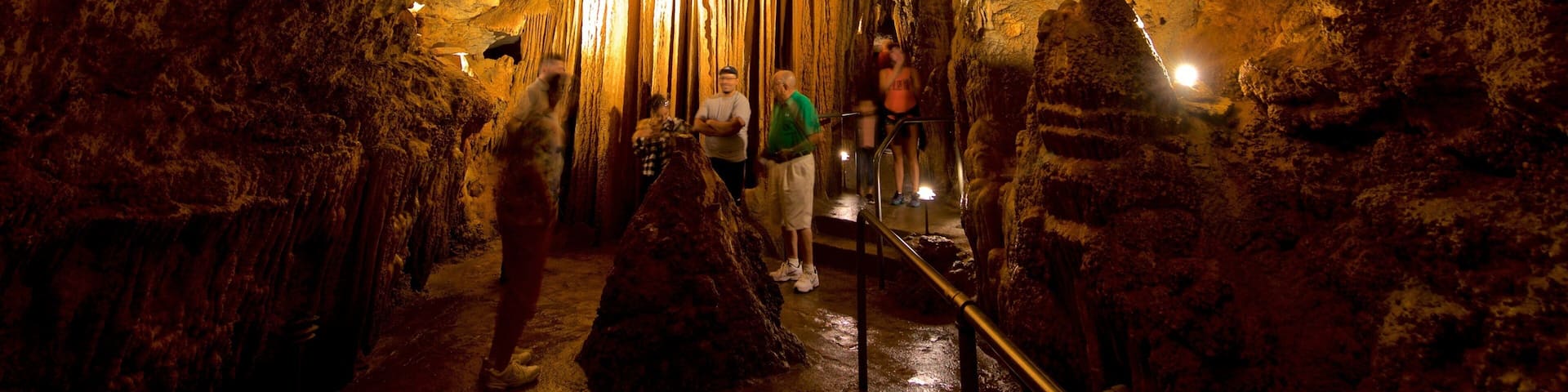 A cave with stalactites and stalagmites, illuminated by artificial lighting.