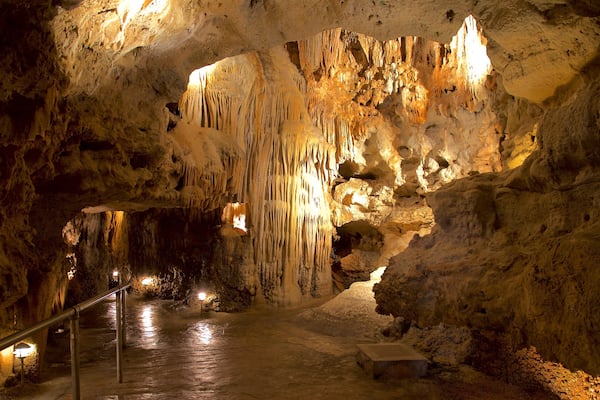 A cave with stalactites and stalagmites, a metal railing, and a bench.