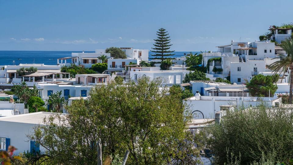 A coastal village with white buildings, a clear blue sea, and lush greenery.