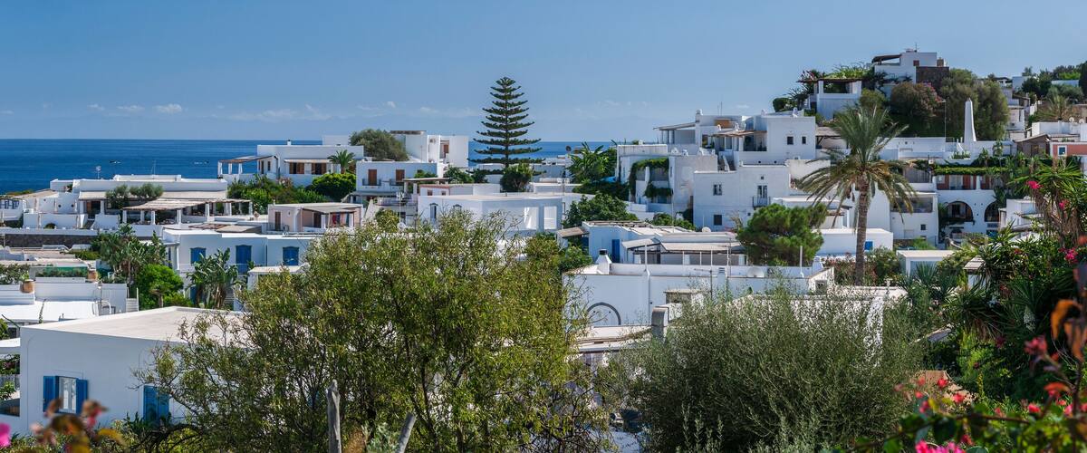 A coastal village with white buildings, a clear blue sea, and lush greenery.