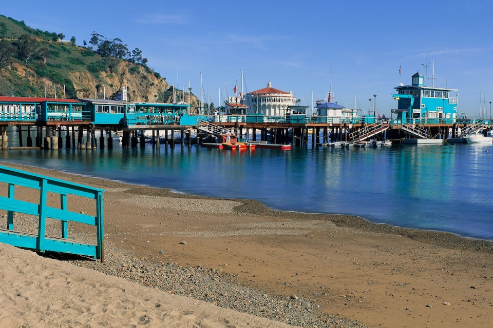 A coastal pier with buildings, boats, and a sandy beach.