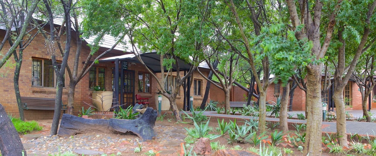 A garden with a large rock, a bench, and a building with a brick facade.