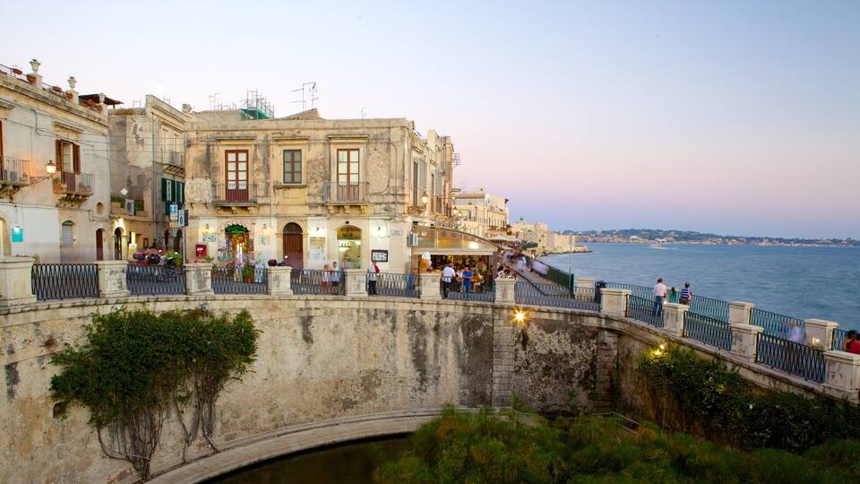 A waterfront promenade with historic buildings, a stone bridge, and a view of the sea.