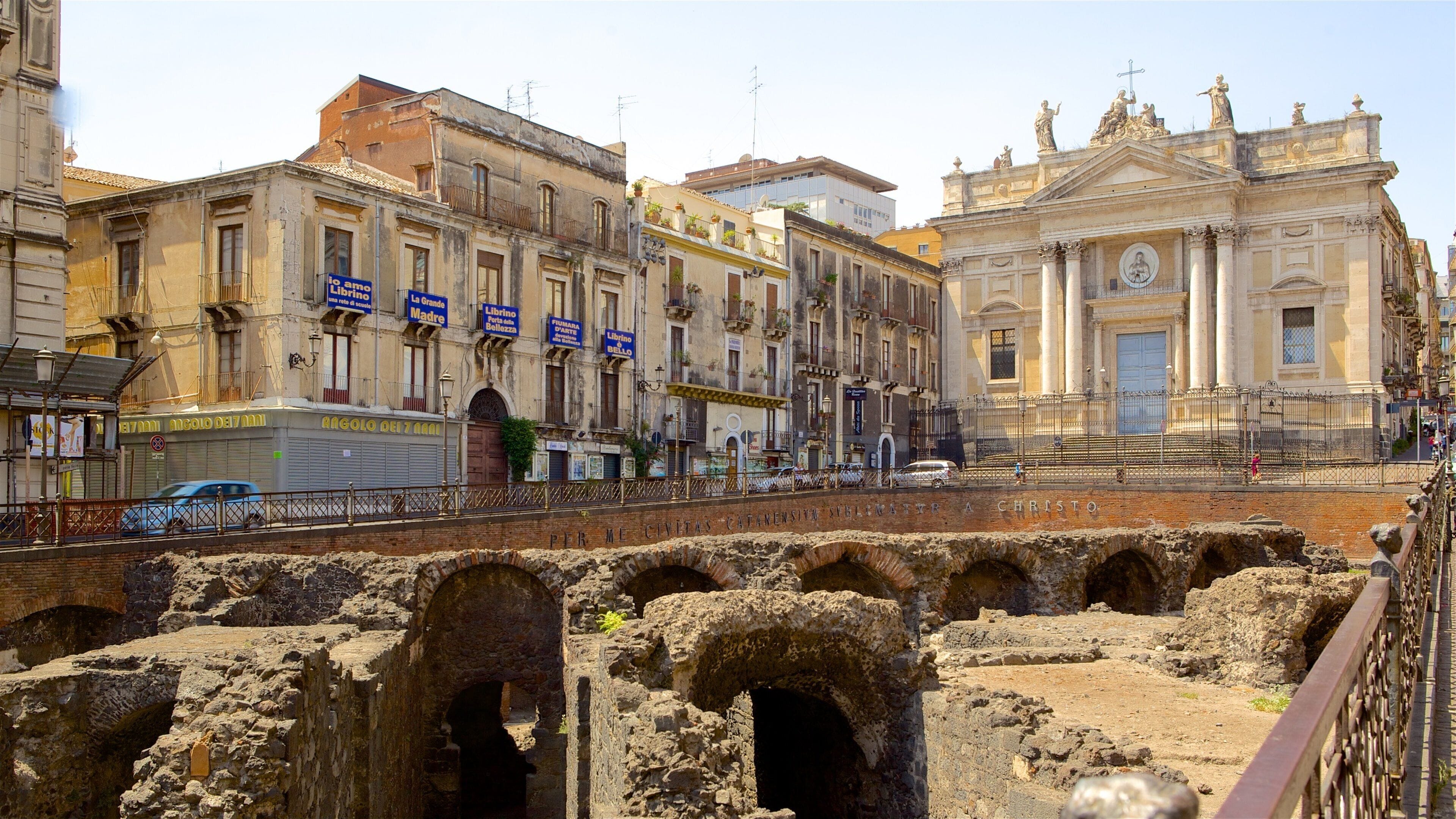 Ancient ruins with arches, a bridge, and historic buildings with signs in a European city.