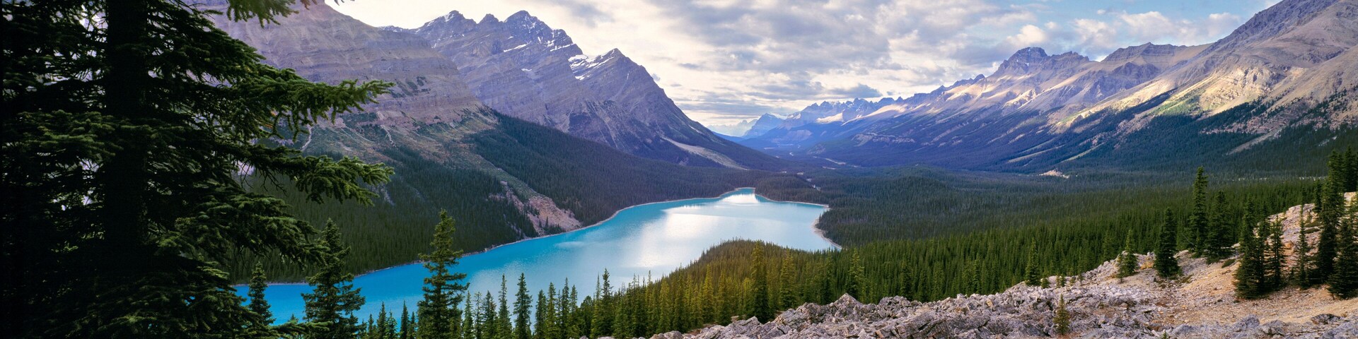 Paisaje montañoso con un lago rodeado de bosques densos y cumbres escarpadas.
