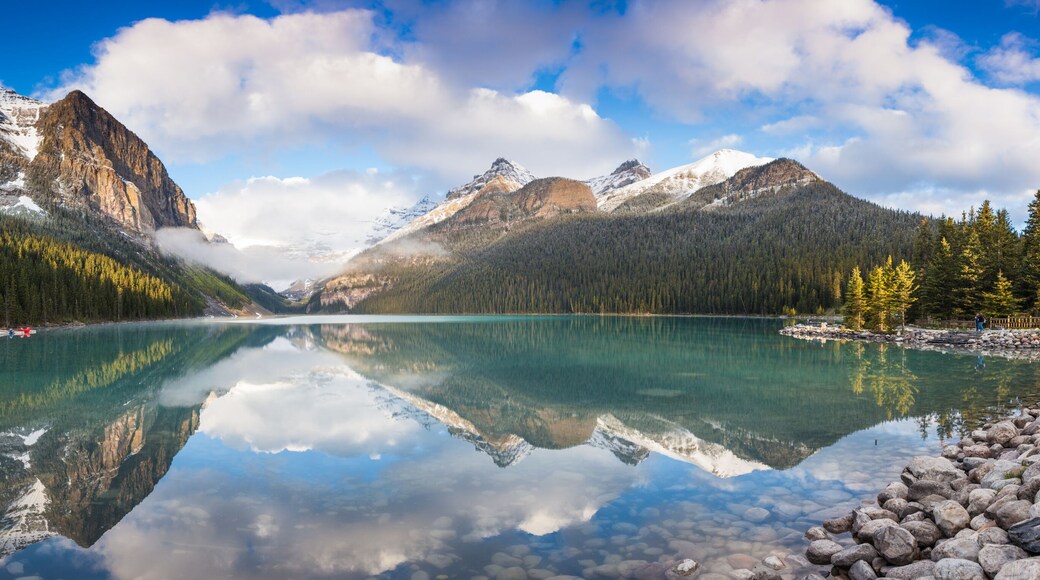 Ein Bergsee mit klaren Spiegelungen, umgeben von bewaldeten Bergen und einer Hütte.