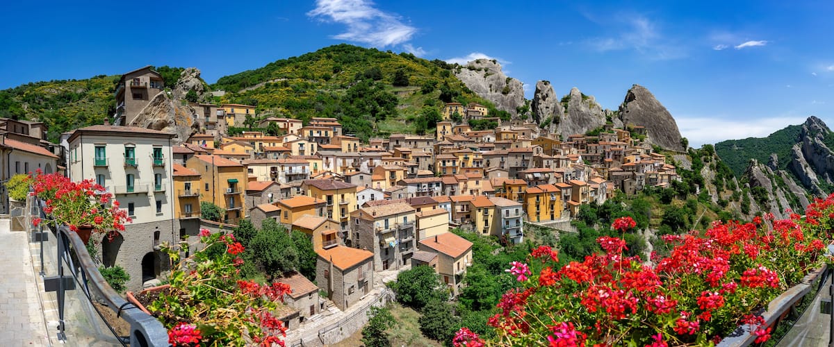 A hillside town with terracotta-roofed buildings, red flowers, and rocky cliffs.