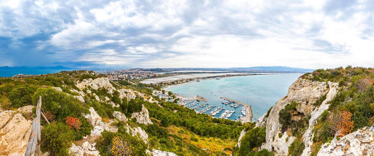 A coastal landscape with rocky cliffs, a marina, and a distant city.