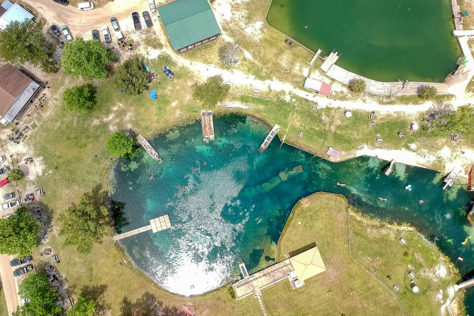 Vista aèria d'un parc amb una gran superfície d'aigua, un parc infantil i edificis als voltants.