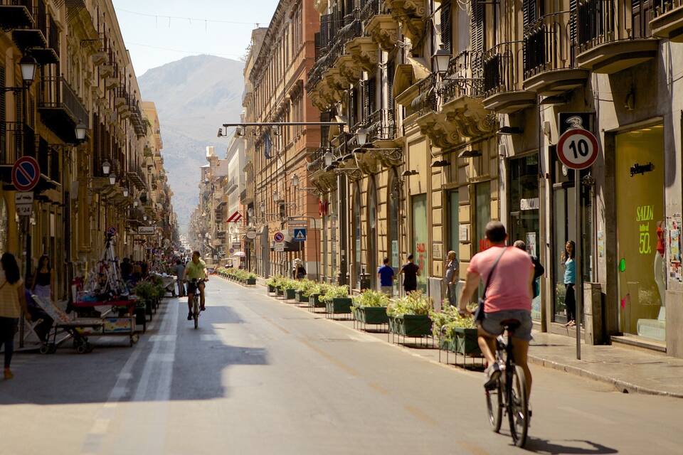 A sunny street with buildings, a cyclist, and pedestrians.