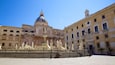 A historic plaza with a fountain, classical statues, and ornate buildings.