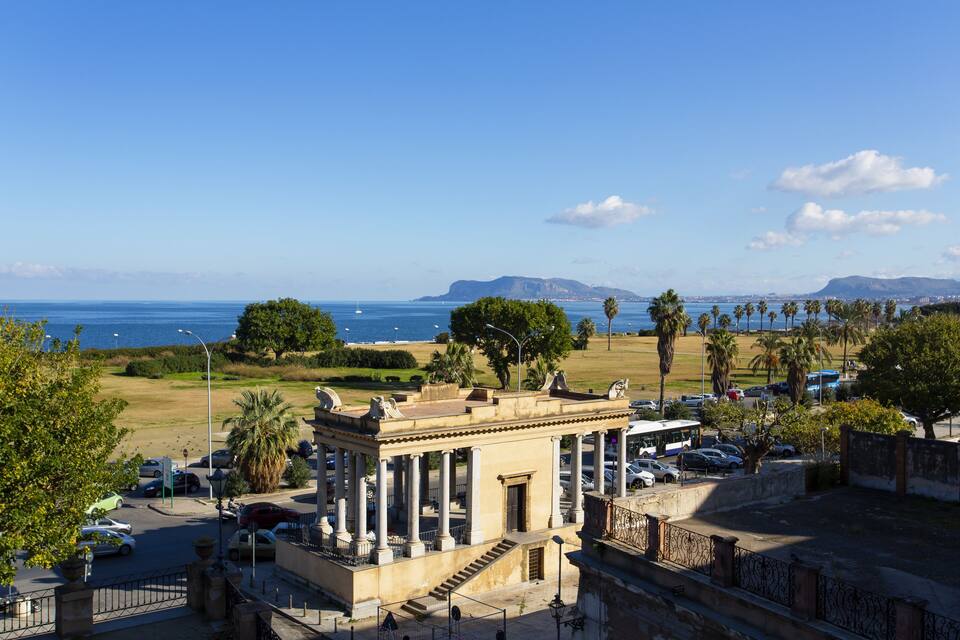 A coastal cityscape with a historic building, palm trees, and a clear blue sky.