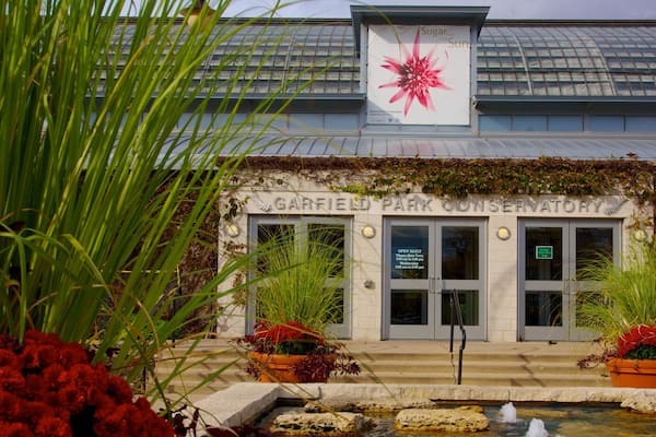 The Garfield Park Conservatory entrance with a signboard, potted plants, and a water feature.