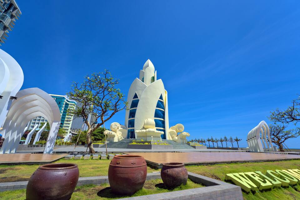 A modern architectural structure with a unique design, surrounded by a landscaped area with large vases and a 'WELCOME' sign.