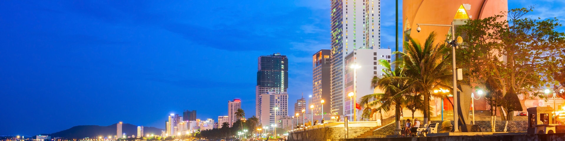 A beach with a distinctive building featuring a pointed top, palm trees, and a city skyline in the background.