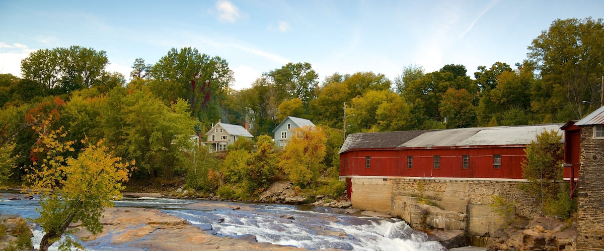 A river flowing through a town with a red mill and houses in the background.