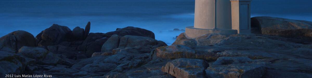A lighthouse on a rocky shore with the ocean in the background.
