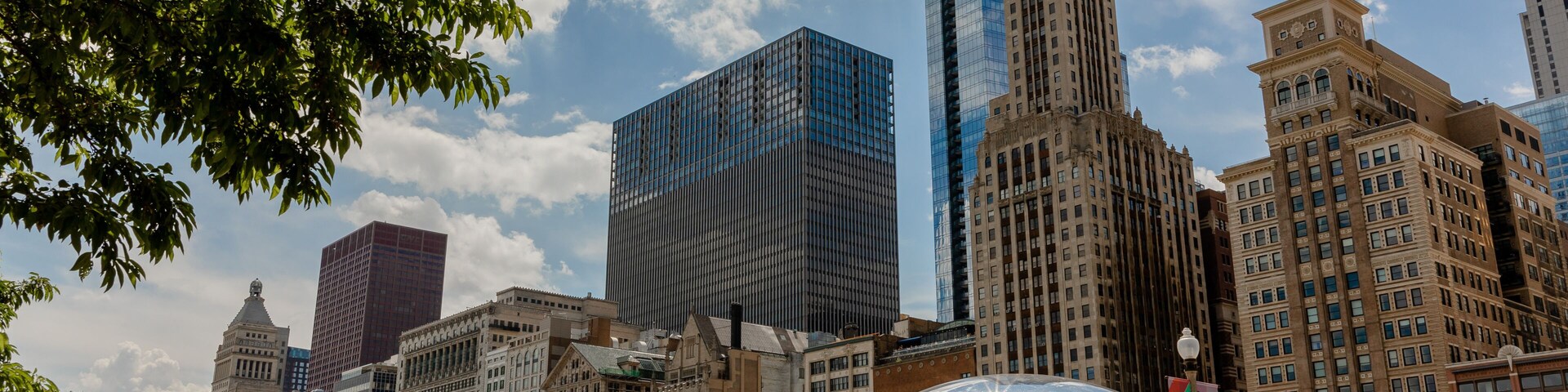 A cityscape with modern skyscrapers, a large reflective sculpture, and a crowd of people in a public square.
