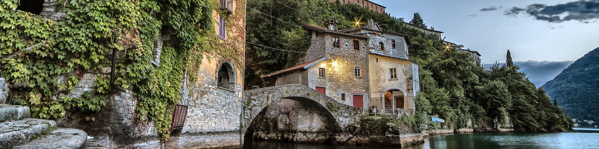 A stone bridge over a calm river, surrounded by lush greenery and historic buildings.