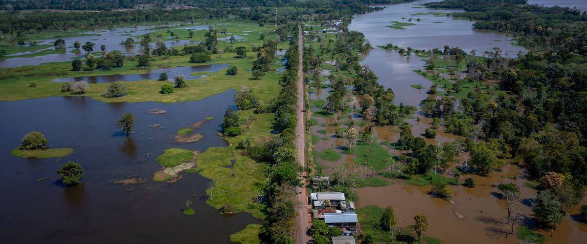 An aerial view of a flooded landscape with a road running through it, surrounded by dense vegetation and water bodies.