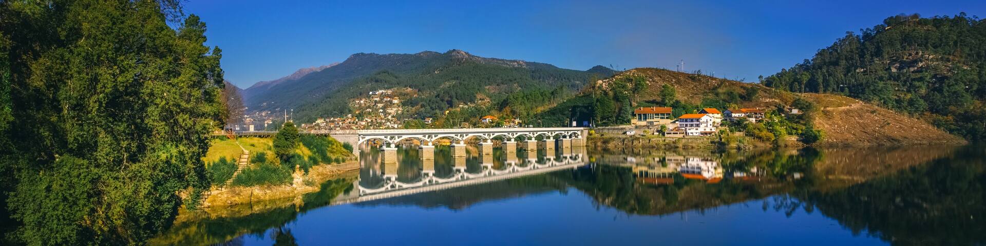 White bridge reflecting in the calm water of the Cavado river, in Rio Caldo, surrounded by lush vegetation and mountains in the peneda geres national park, terras de bouro, portugal,