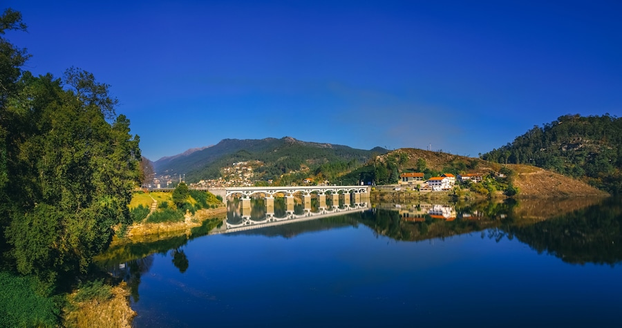 White bridge reflecting in the calm water of the Cavado river, in Rio Caldo, surrounded by lush vegetation and mountains in the peneda geres national park, terras de bouro, portugal,