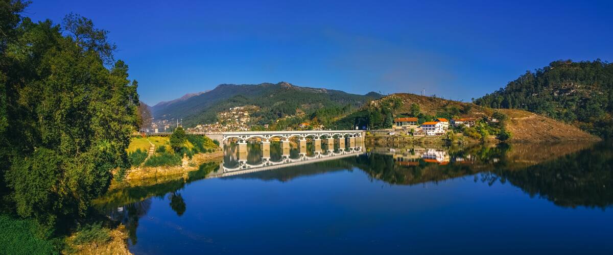 A bridge over a calm river, surrounded by lush greenery and hills.