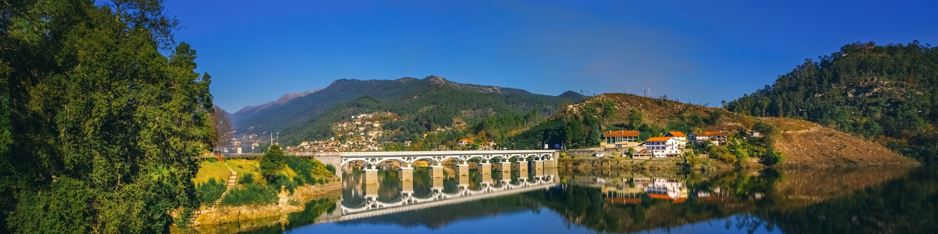 A bridge over a calm river, surrounded by lush greenery and hills.