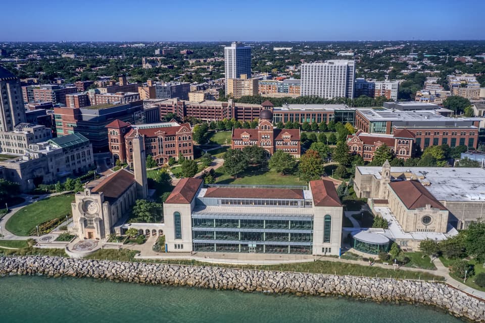 An aerial view of a university campus with historic buildings, a large modern library, and a waterfront.