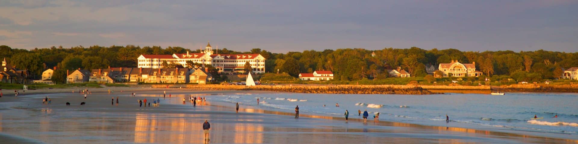 A beach with people, a large building, and a forest in the background.