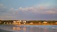 En strand med mennesker, en stor bygning og en skov i baggrunden.