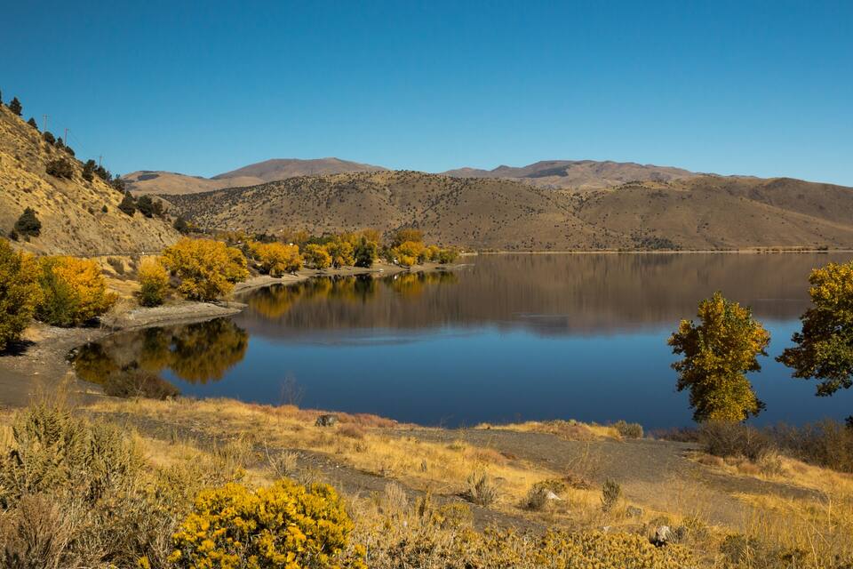 A calm lake surrounded by hills and autumn-colored trees.