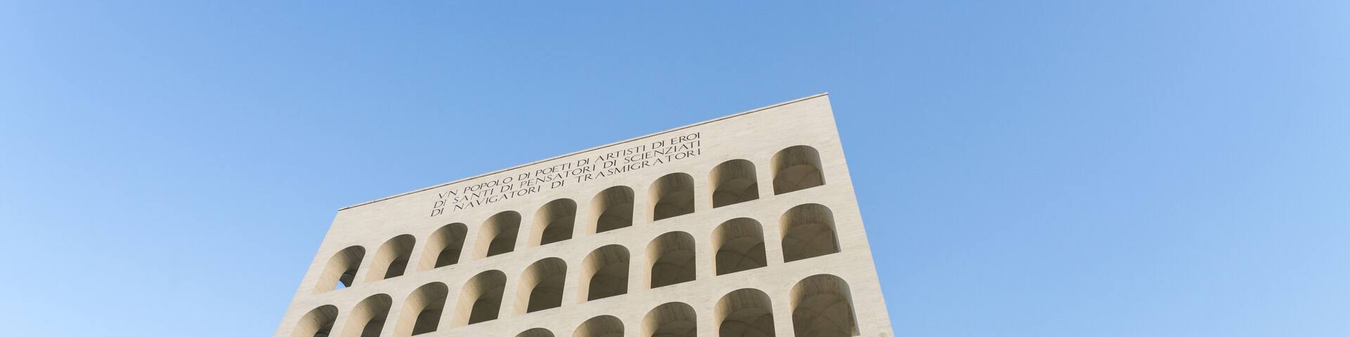 View of Palazzo della Civiltà Italiana rises with stark arches against a clear sky, its stark white facade softened by the warm sunlight, Rome, Lazio, Italy.