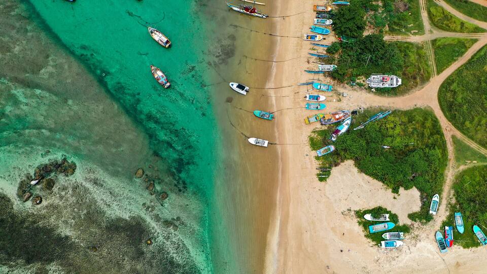 Sri Lankan coastal life captured from above—Weligama Beach with traditional boats, palm forest, and serene ocean vibes.