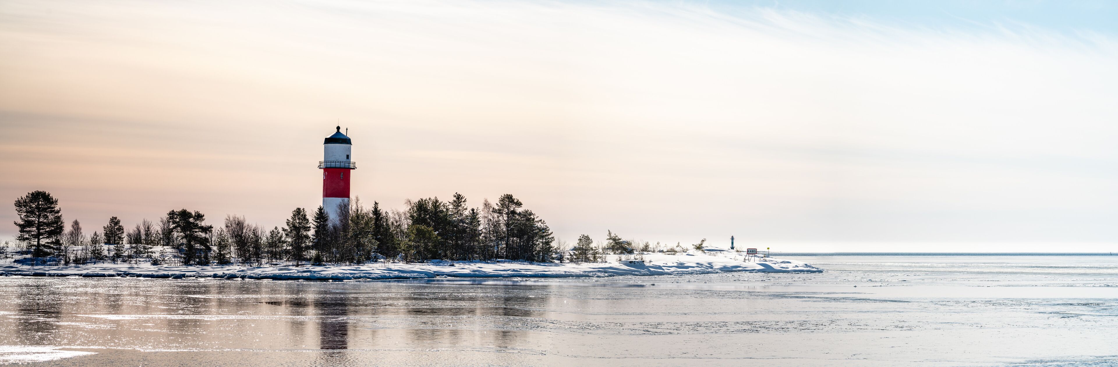 A lighthouse on a snowy island with a frozen sea in the foreground.