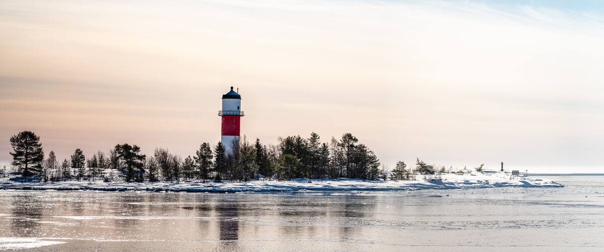 A lighthouse on a snowy island with a frozen sea in the foreground.