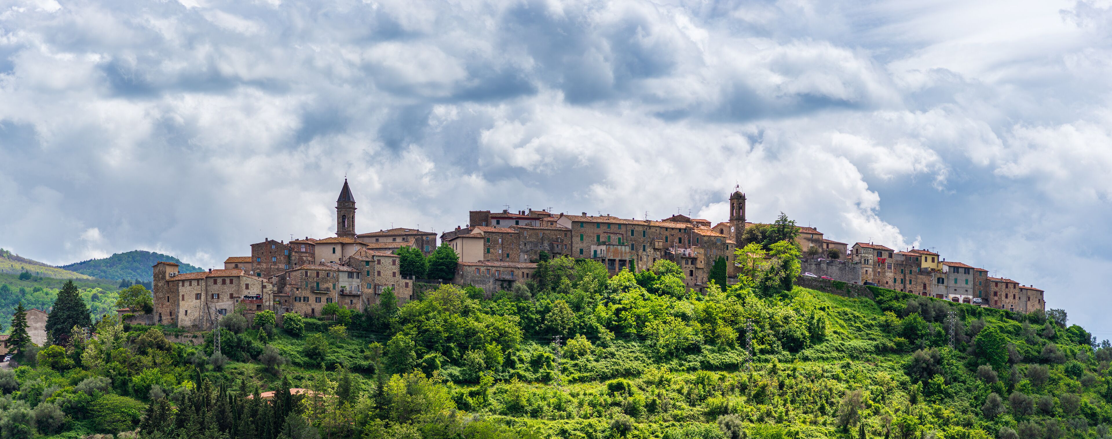 A historic town perched on a hillside with dense greenery and a cloudy sky.