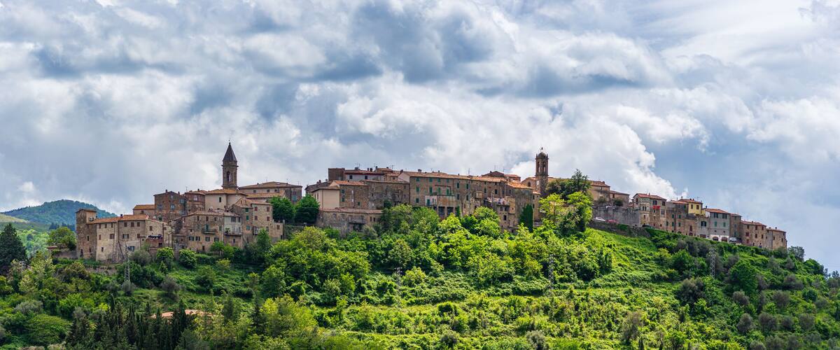 A historic town perched on a hillside with dense greenery and a cloudy sky.