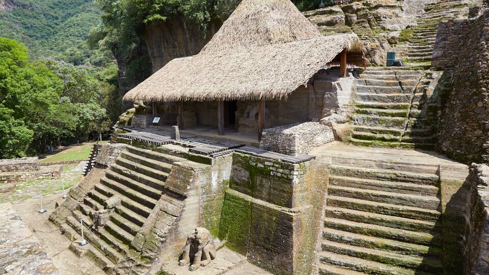 A stone staircase leading to a thatched-roof structure amidst a lush green valley.