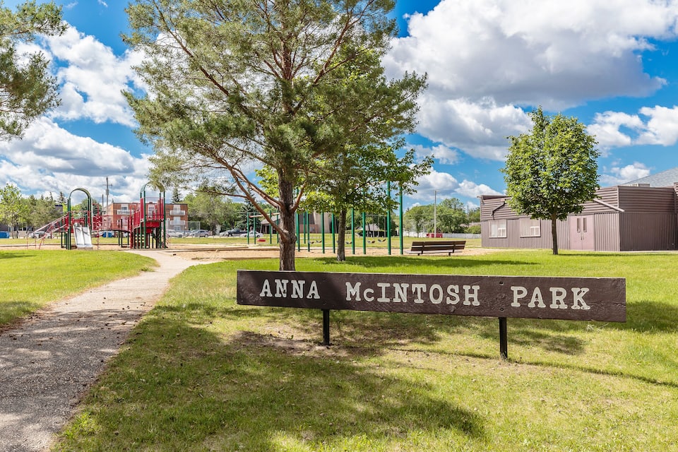 A park sign reading "Anna McIntosh Park" with playground equipment and trees in the background.