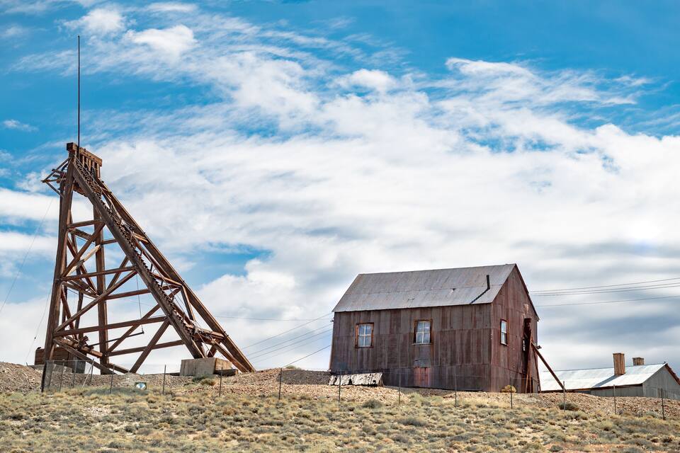 A rusted wooden structure and a dilapidated building in a desert landscape.