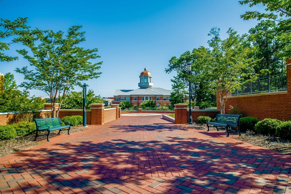 A brick pathway leading to a building with a dome and a clock tower.