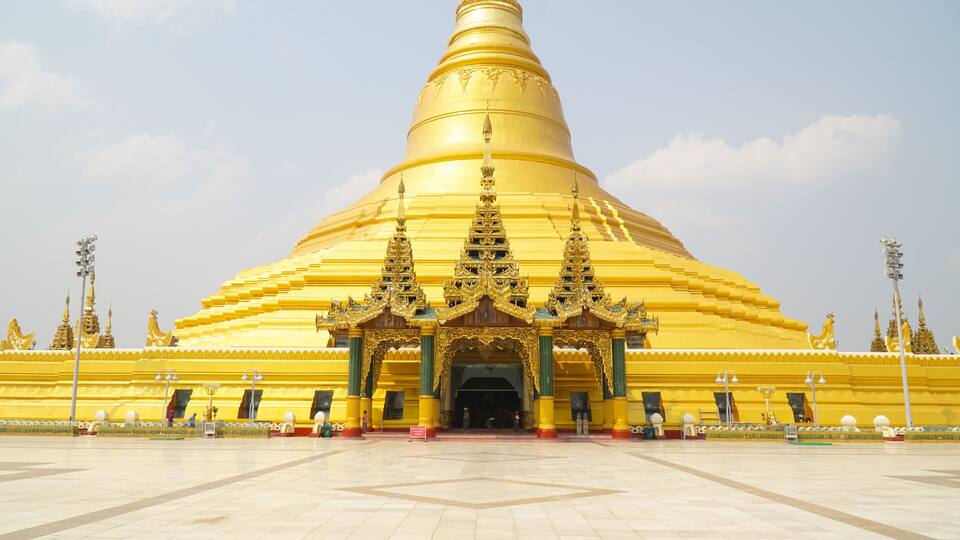 A large golden stupa with intricate architecture and a tiled courtyard.