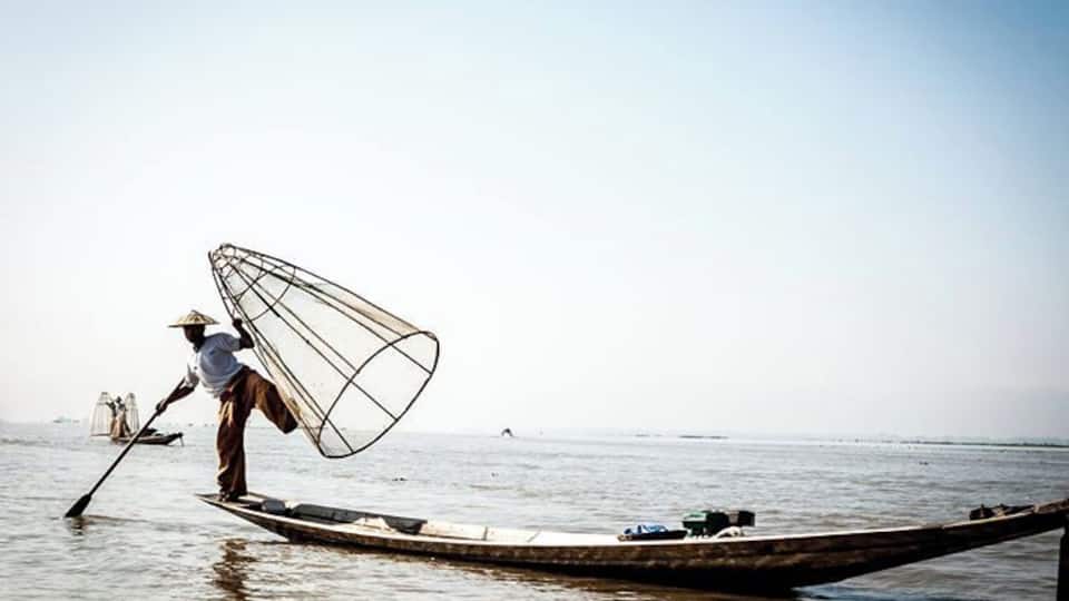 A person on a boat using a large fishing net in a calm body of water.